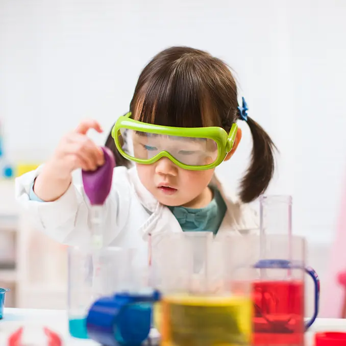 Child wearing safety goggles using a dropper during a STEAM activity